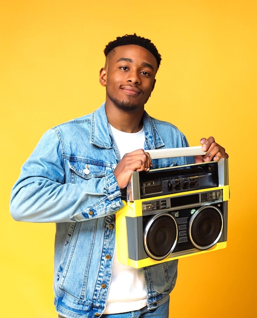 foto jovem bonito vestindo jaqueta jeans segurando boombox em fundo amarelo