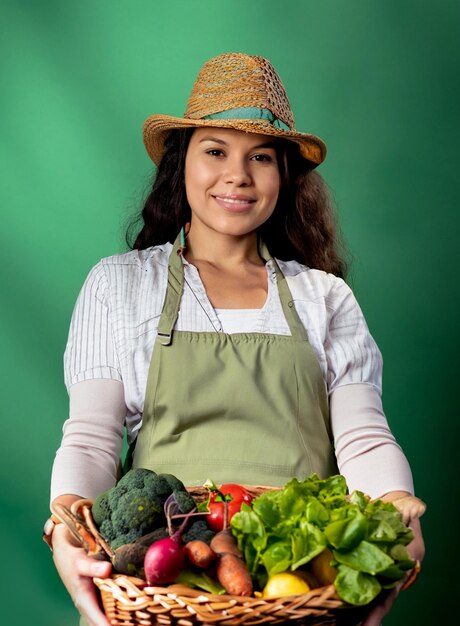 Foto foto jovem mulher bonita jardineiro em avental e chapéu segurando cesta cheia de vegetais