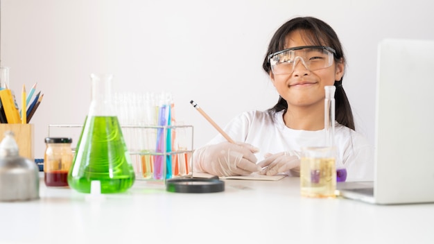 Foto de joven adorable escribiendo un resultado de química en el libro mientras realiza un experimento científico