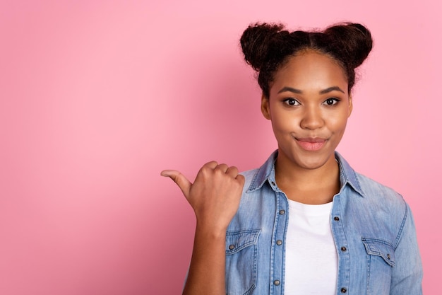 La foto de una joven africana indica que el espacio vacío del pulgar es una oferta promocional que sugiere una elección aislada sobre un fondo de color rosa