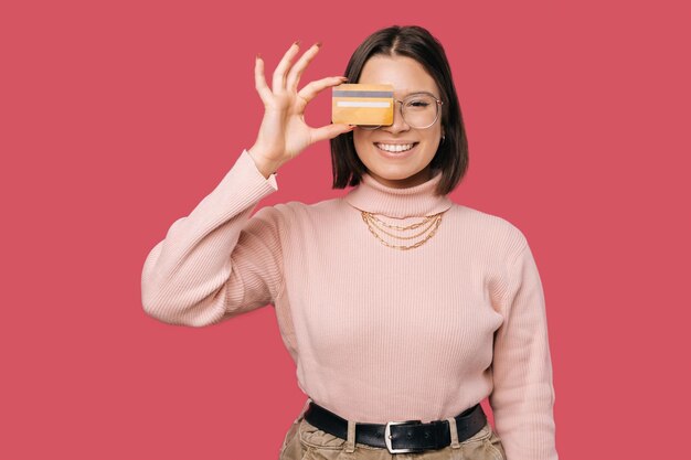 Foto foto de una joven y alegre mujer de moda sosteniendo una tarjeta de crédito amarilla sobre los ojos y mirando la cámara