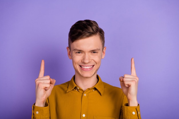 Foto de un joven alegre que indica una propuesta de descuento de espacio vacío con los dedos aislada sobre un fondo de color violeta