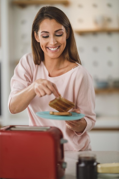 Una foto de una joven asando una tostada en una tostadora para desayunar en casa.