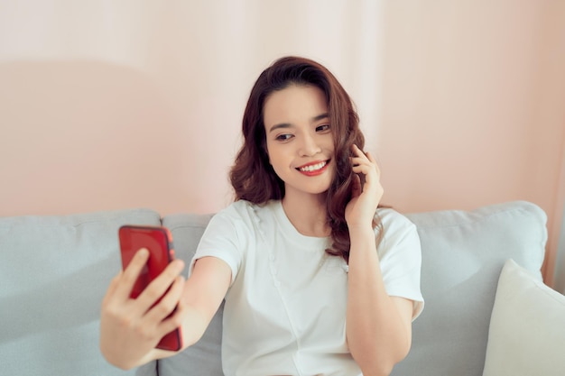 Una foto de una joven asiática feliz tomándose selfie con su celular mientras estaba sentada en la sala de estar.