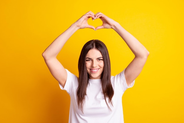 Foto de joven atractiva muestra los dedos corazón símbolo sentimientos amor romance aislado sobre fondo de color amarillo