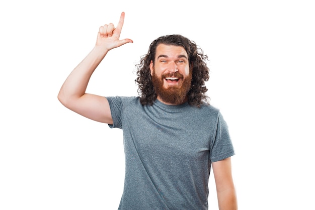 Foto de joven barbudo con cabello largo sonriendo y apuntando hacia arriba con el dedo