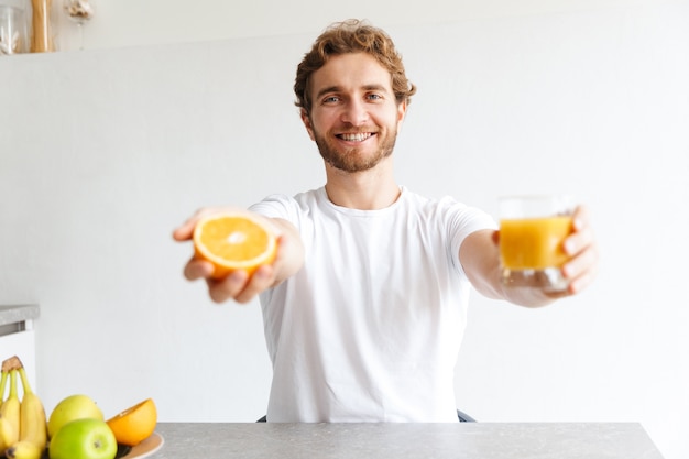 Foto de un joven barbudo feliz en la mesa en casa con frutas.