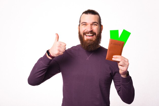 La foto de un joven barbudo sosteniendo un pasaporte con dos boletos muestra un pulgar hacia arriba y sonriendo