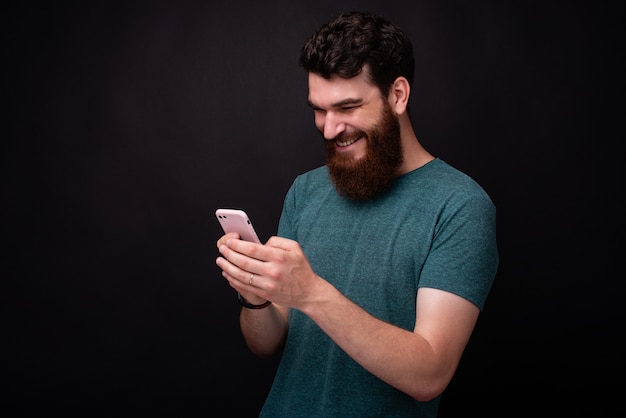 Foto de joven barbudo usando su teléfono inteligente y sonriendo