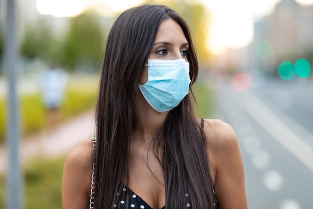 Foto de una joven y bella mujer de pie mascarilla en la calle.