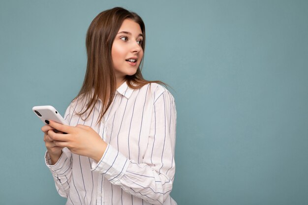 Foto de la joven y bella mujer rubia con camisa blanca casual aislado sobre la pared de fondo azul