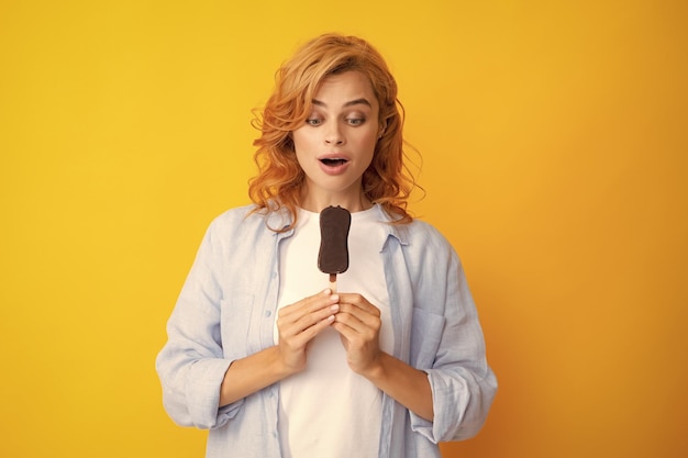 La foto de una joven come un delicioso helado disfruta de un postre congelado vestida con ropa informal aislada en un fondo amarillo