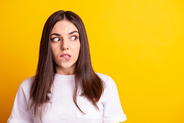 Foto de una joven dama bonita que muerde los labios se pregunta mirar el espacio vacío asustado preocupado mirar el espacio vacío aislado sobre el fondo de color amarillo