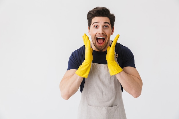 Foto de un joven emocionado con guantes de goma amarillos para la protección de las manos sonriendo mientras limpia la casa aislada sobre blanco