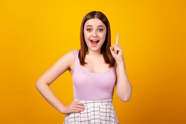 La foto de una joven encantadora tiene idea de indicar con el dedo que elija una solución de decisión aislada sobre un fondo de color amarillo