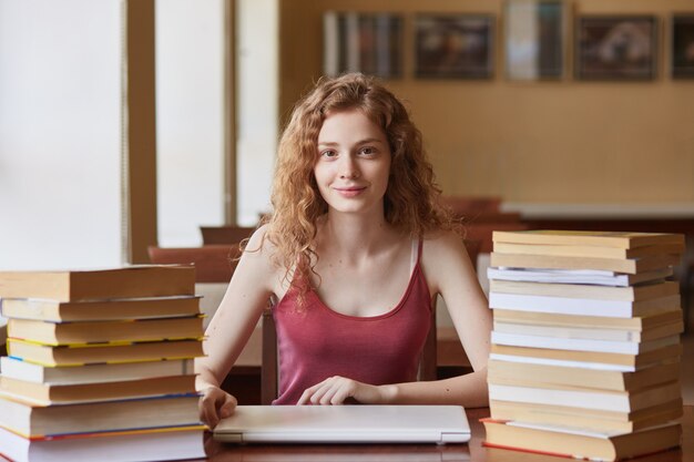 Foto de joven estudiante de pelo astuto sentado a la mesa en la biblioteca