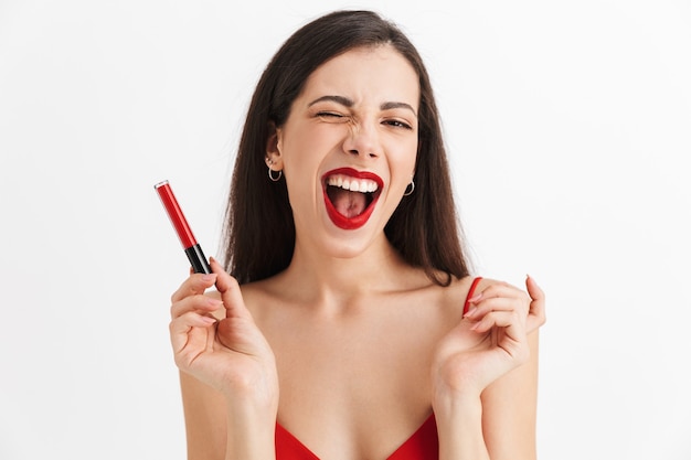 Foto de joven feliz emocionada posando aislado sosteniendo brillo de labios haciendo maquillaje.