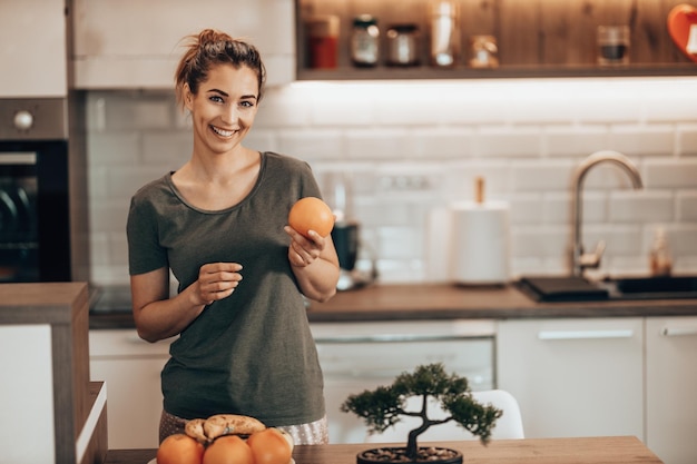 Una foto de una joven feliz preparando un desayuno de frutas en la cocina de su casa. Mirando a la cámara.