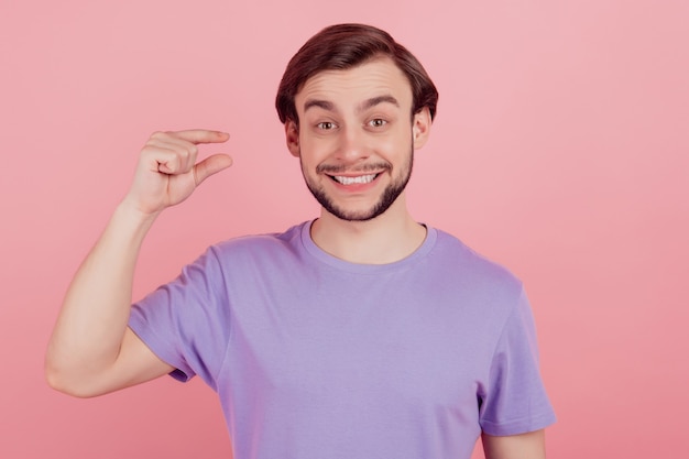 Foto de joven feliz sonrisa positiva muestran diminutas medidas de tamaño pequeño con los dedos aislados sobre fondo de color rosa