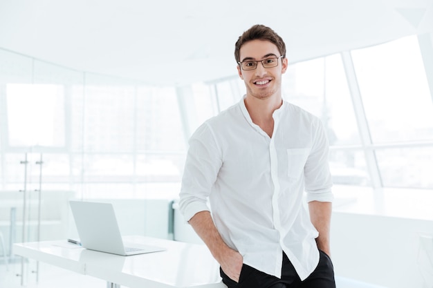 Foto foto de joven feliz vestido con camisa blanca de pie sobre fondo de ventana blanca grande. mirando a la cámara.