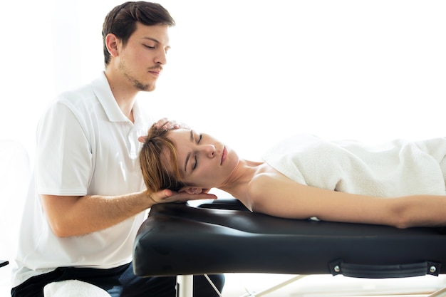 Foto de joven fisioterapeuta haciendo un tratamiento de cuello al paciente en una sala de fisioterapia. Rehabilitación, masaje médico y concepto de terapia manual.