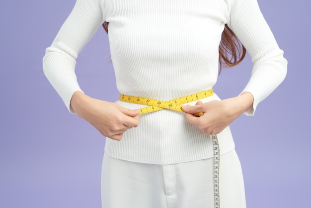 Foto de una joven en forma y saludable que mide su cintura con una cinta métrica en centímetros y milímetros.