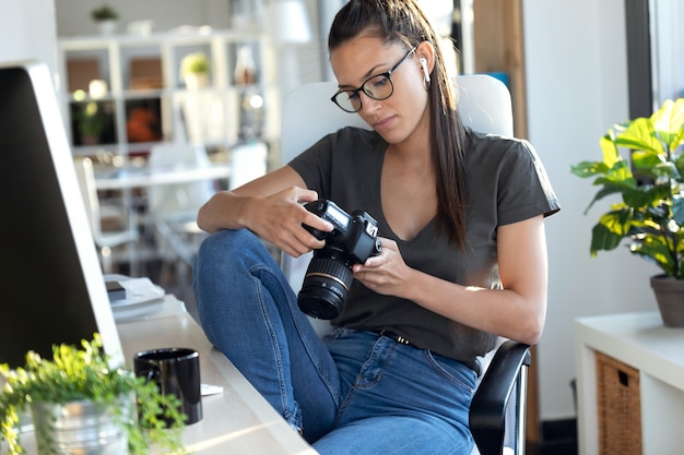 Foto de joven fotógrafo profesional revisando las fotos que ha tomado con la cámara mientras está sentada en el estudio.