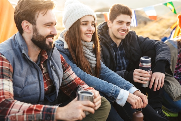 Foto de un joven grupo de amigos al aire libre en vacaciones alternativas gratuitas acampando sobre las montañas bebiendo té caliente hablando entre sí.