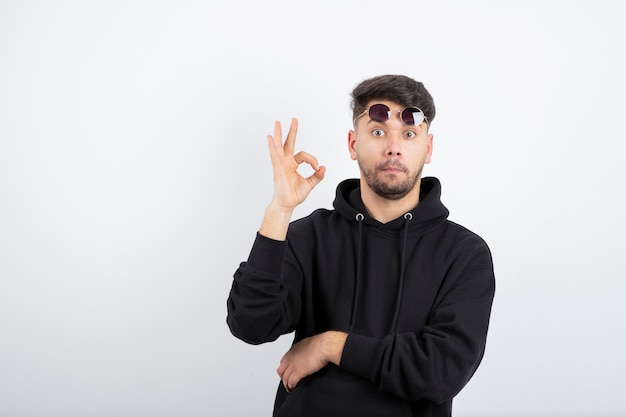 Foto de joven guapo con gafas de pie y dando señal de ok