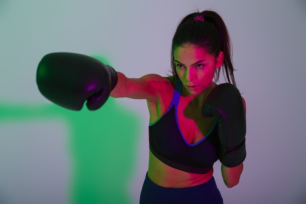 Foto de joven hermosa hermosa mujer fuerte fitness boxeador aislado con luces de flash led hacer ejercicios de boxeo en guantes.