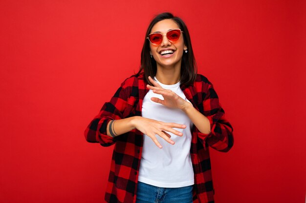 Foto de joven hermosa mujer morena sonriente feliz vistiendo camiseta blanca de moda y cheque rojo