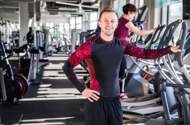 Foto de joven - instructor de fitness sonriendo y mirando a la cámara en el fondo del gimnasio