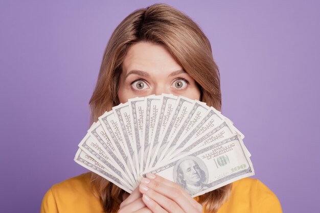 Foto de joven mujer bonita cara de cierre montón de dinero en efectivo rico aislado sobre fondo de color violeta