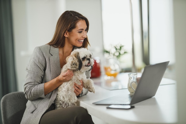 Una foto de una joven mujer de negocios sentada con su perro mascota y usando su laptop durante el trabajo desde casa.