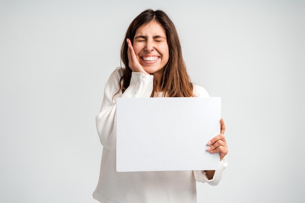 Foto de joven mujer positiva feliz sosteniendo vallas publicitarias vacías para elegir asesoramiento aislado sobre fondo de color blanco