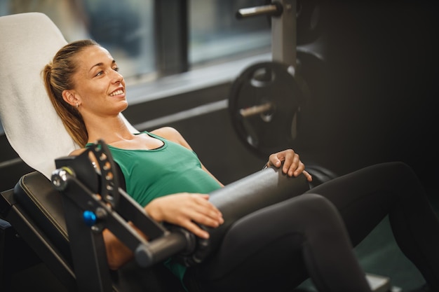 Una foto de una joven musculosa con ropa deportiva haciendo ejercicio en el gimnasio. Ella está haciendo ejercicio de puente de glúteos para su glúteo en la máquina de confianza de cadera.