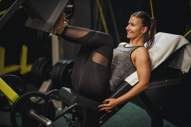 Foto una foto de una joven musculosa con ropa deportiva haciendo ejercicio en el gimnasio. ella está haciendo ejercicios para sus piernas en una máquina de prensa de piernas.