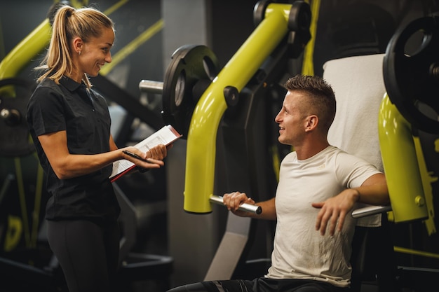 Foto una foto de una joven musculosa con ropa deportiva trabajando con un entrenador personal en la máquina del gimnasio. ella está bombeando su músculo pectoral con mucho peso.