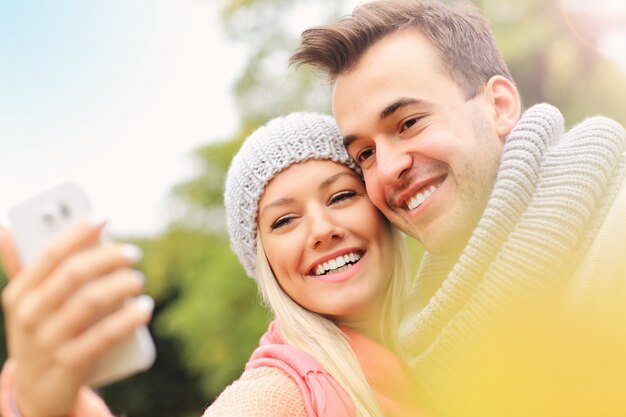 Una foto de una joven pareja romántica con smartphone en el parque en otoño