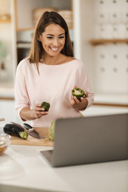 Foto una foto de una joven sonriente preparando una comida saludable y haciendo un blog de video en una laptop en casa.