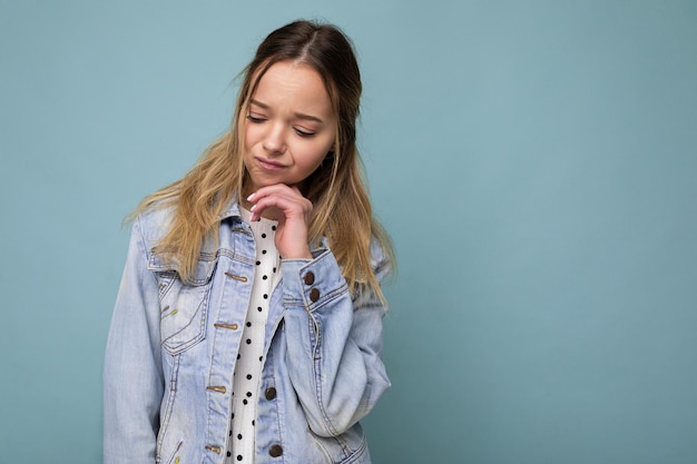 Foto de joven triste molesta hermosa mujer rubia con emociones sinceras vistiendo chaqueta azul de mezclilla