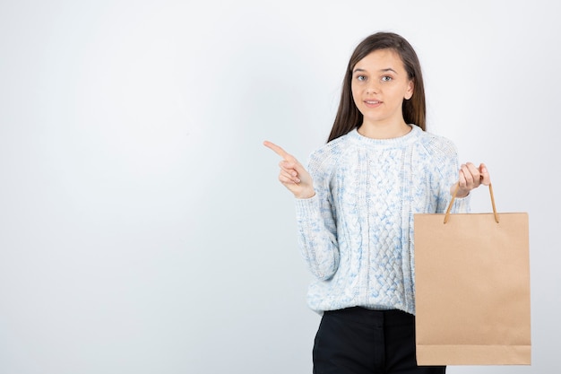 Foto de jovencita en suéter con bolsa de artesanía posando para la cámara.