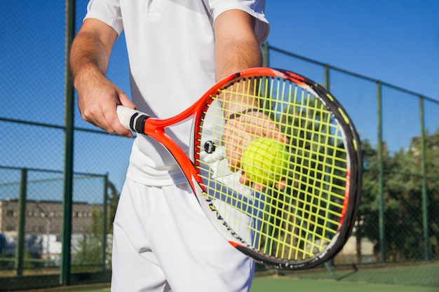 Foto de jugador de tenis profesional de cerca con una raqueta y una pelota de tenis.