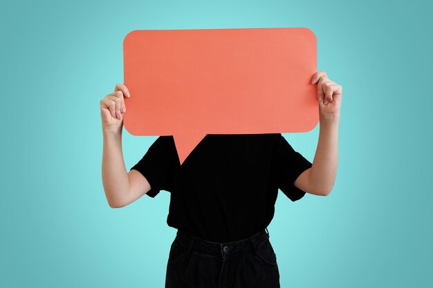 Foto foto junge frau mit orangefarbenem plakat der sprechblase, das ihr gesicht isoliert auf blauem hintergrund bedeckt