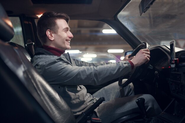 Foto del lado del joven sonriente sentado en el coche