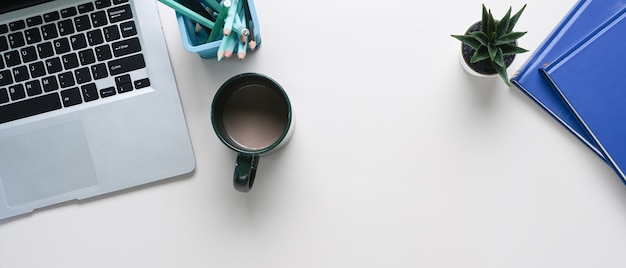 Foto laicos plana de la mesa de escritorio de oficina blanca con cuaderno, computadora portátil, taza de café, papelería y espacio de copia.