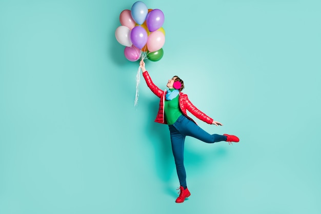 Foto lateral de perfil de corpo inteiro de menina alegre positiva aproveite férias de outono pegar vento voando muitos balões de hélio usam calçados de jumper verde rosa isolados sobre parede de cor azul-petróleo