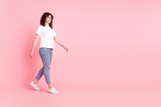 Foto lateral de perfil em tamanho real de uma jovem adorável ir passear e olhar o espaço vazio isolado sobre um fundo de cor rosa