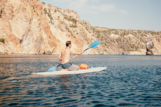 Foto lateral de um homem nadando e relaxando no supboard homem esportivo no mar na arquibancada