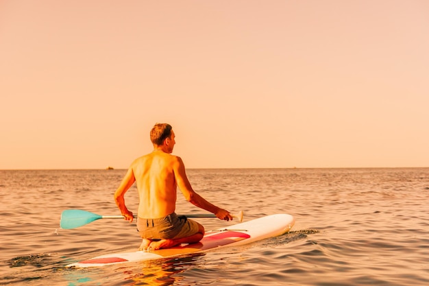 Foto lateral de um homem nadando e relaxando no supboard homem esportivo no mar na arquibancada